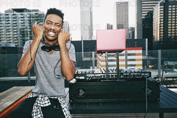 Black DJ biting headphones cord on urban rooftop