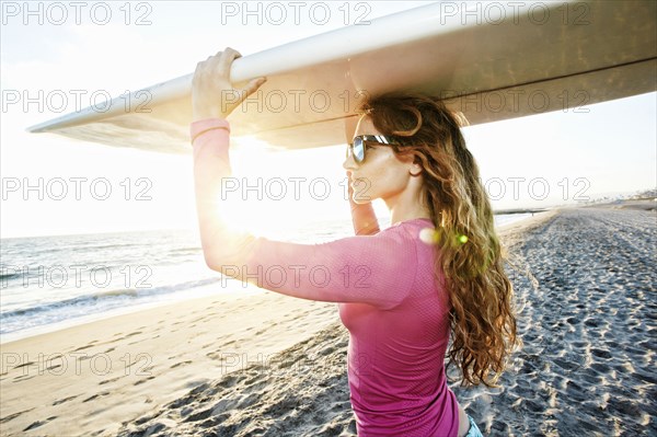 Caucasian woman carrying surfboard on beach