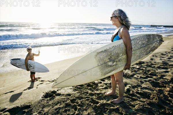 Older Caucasian couple standing on beach with surfboards