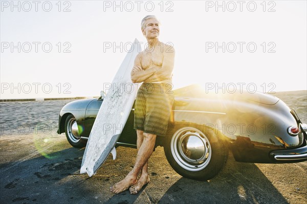 Older Caucasian man on leaning on convertible car with surfboard