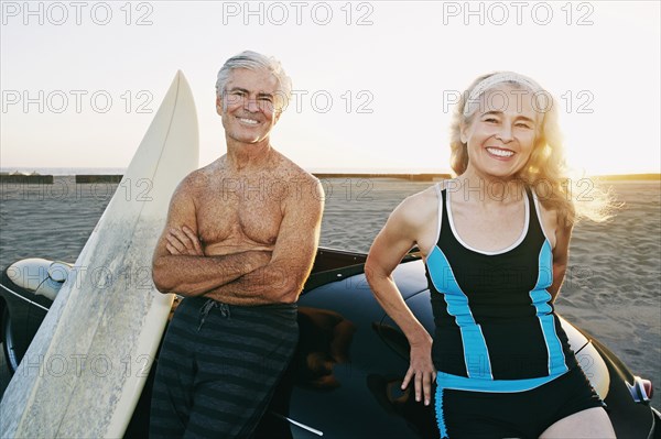 Older Caucasian couple leaning on convertible car with surfboards