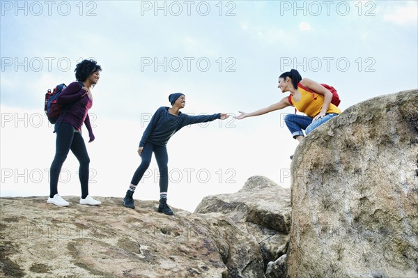 Woman helping friend hiking on rock formation