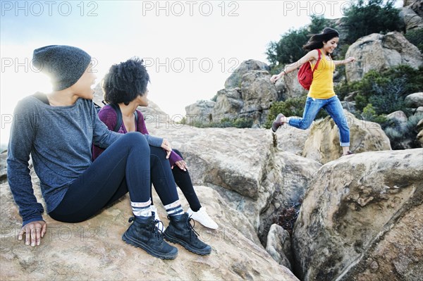 Women watching friend jumping on rock formation