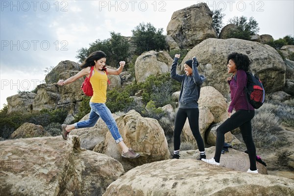 Women cheering friend jumping on rock formation