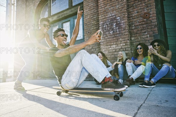 Woman pushing friend sitting on skateboard in city