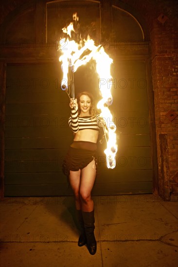 Caucasian woman juggling fire on city sidewalk at night