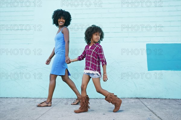 Smiling mother and daughter walking on sidewalk