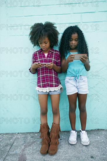 Girls leaning on wall texting on cell phones