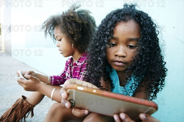 Girls sitting on sidewalk texting on cell phones
