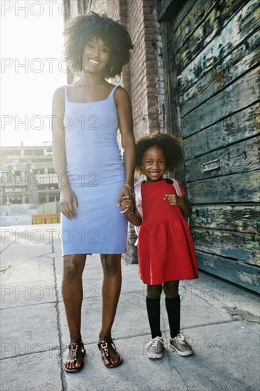 Portrait of smiling mother and daughter standing on sidewalk