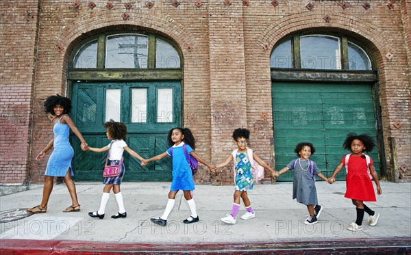 Woman leading girls holding hands on city sidewalk