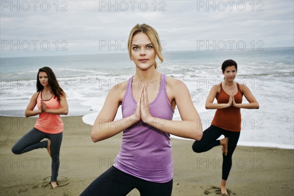 Caucasian women performing yoga on beach