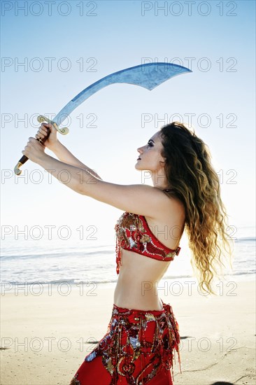 Caucasian belly dancer holding sword on beach