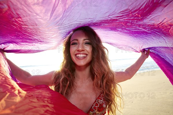 Caucasian belly dancer posing under scarf on beach