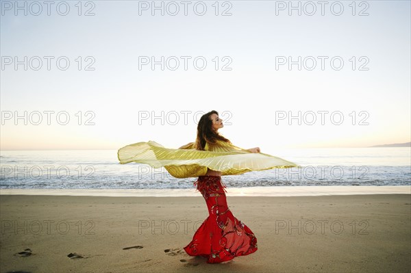 Caucasian belly dancer twirling cape on beach