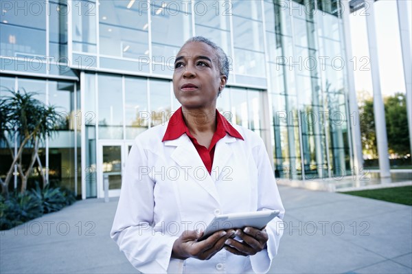 Portrait of serious African American doctor holding digital tablet outdoors