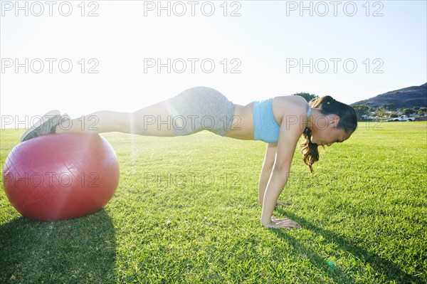 Mixed Race woman balancing on fitness ball doing push-ups