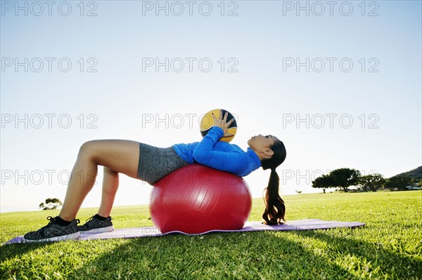 Mixed Race woman exercising with fitness ball and heavy ball in sunny field