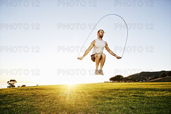 Caucasian man jumping rope in sunny field