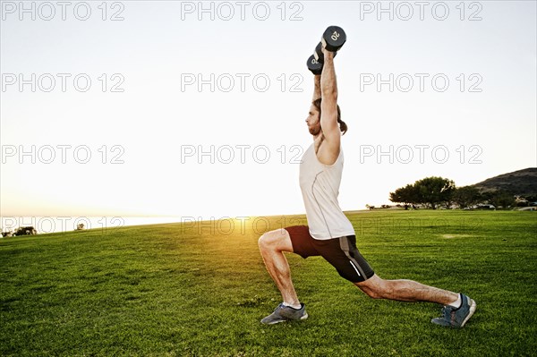 Caucasian man lifting dumbbells in sunny field