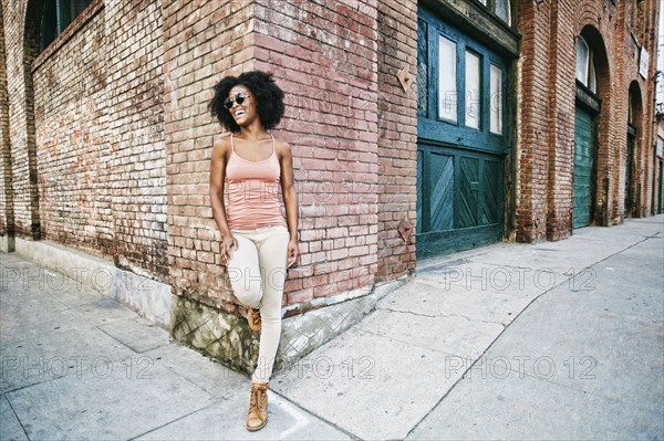 Laughing Black woman leaning on corner of brick building