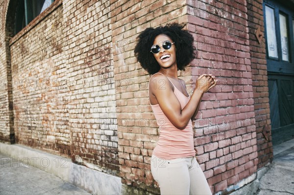 Laughing Black woman standing near corner of brick building