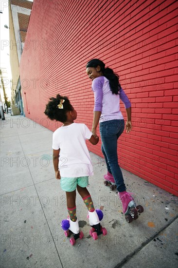 Black mother and daughter wearing roller skates holding hands