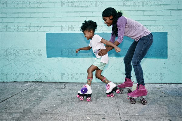 Black mother holding waist of daughter wearing roller skates