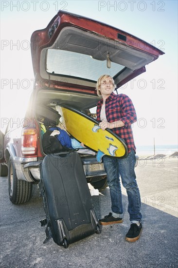 Caucasian man unloading surfboard from car hatch