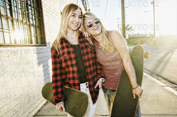 Smiling Caucasian women holding skateboards on sidewalk