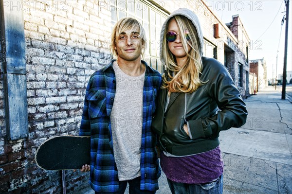 Caucasian couple with skateboard posing on urban sidewalk