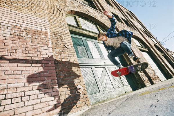 Caucasian man jumping on skateboard on urban sidewalk