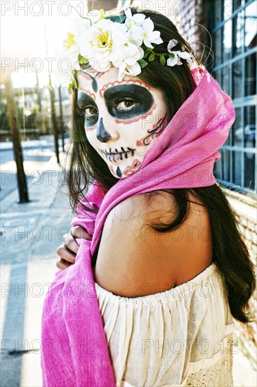 Mixed Race woman on sidewalk wearing scarf and skull face paint
