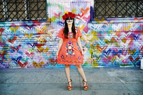 Hispanic woman standing on sidewalk wearing skull face paint