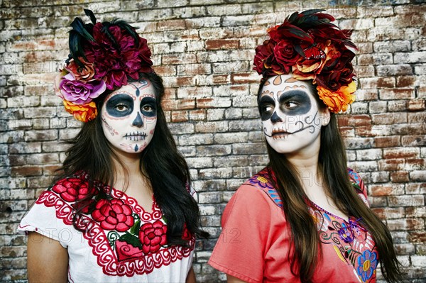 Women near brick wall wearing skull face paint