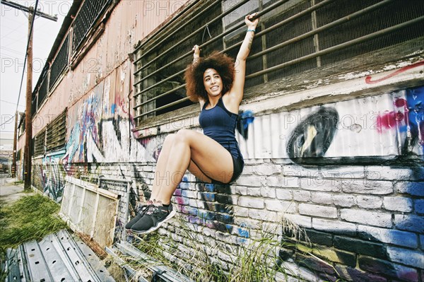 Hispanic woman hanging on bar on graffiti wall