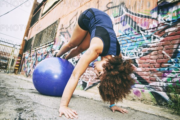 Hispanic woman balancing on fitness ball near graffiti wall