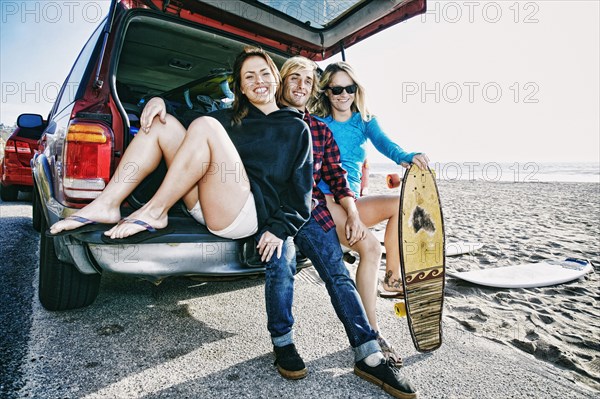 Caucasian friends sitting in car hatch with skateboard