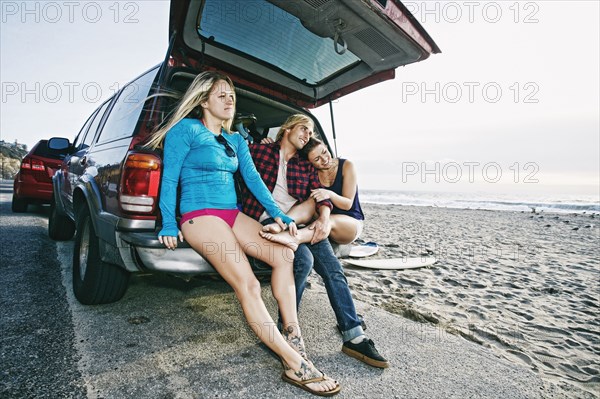 Caucasian friends sitting in car hatch at beach