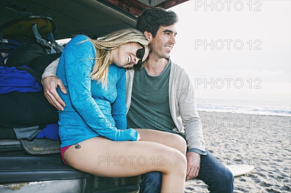 Caucasian couple sitting in car hatch at beach