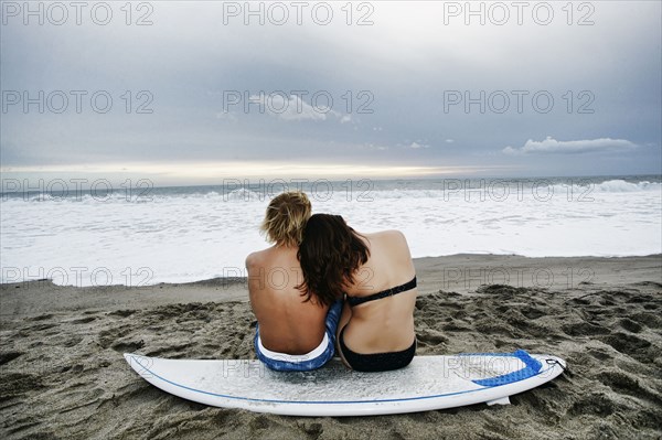 Caucasian couple sitting on surfboard at beach