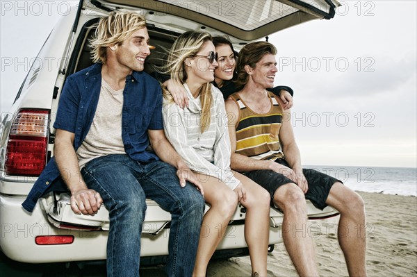 Caucasian friends sitting in car hatch at beach