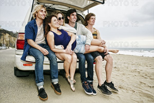 Caucasian friends sitting in car hatch at beach