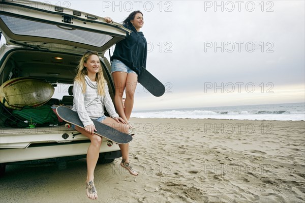 Caucasian women in car hatch at beach holding skateboards