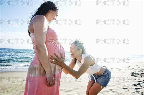 Woman holding belly of expectant mother at beach