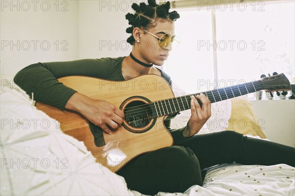 Mixed Race woman sitting on bed playing guitar
