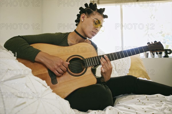 Mixed Race woman sitting on bed playing guitar