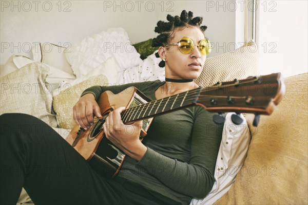 Mixed Race woman sitting on bed playing guitar