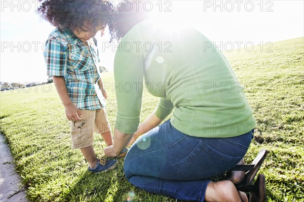 Mixed race mother tying shoe of son