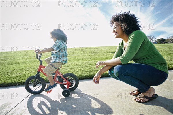 Mixed race mother watching son ride bicycle